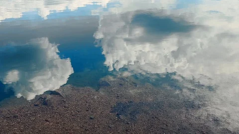 Reflection of clouds in a blue lake with a shore with small stones Stockbeeldmateriaal 129728378