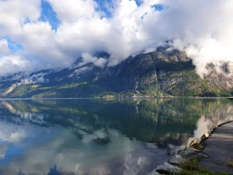Reflection of the cloudy sky and mountains in the water of the fjord - Eidfjord Stock Photos