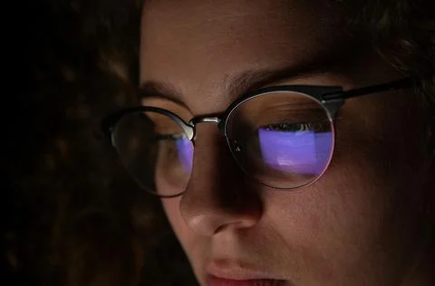 Reflection of a computer screen in glasses of a woman who is working at night Stock Photos