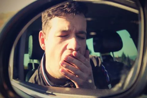 Reflection of the driver in the rear-view mirror. He`s tired and yawns. Stock Photos