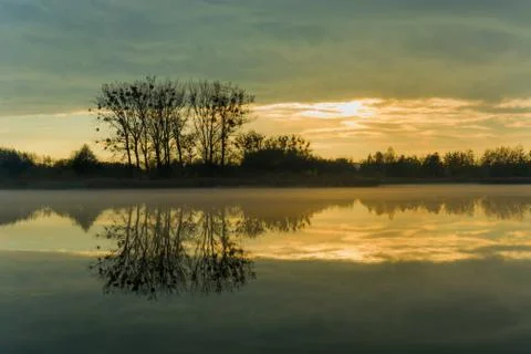 Reflection of evening clouds and trees in a misty lake Stock Photos