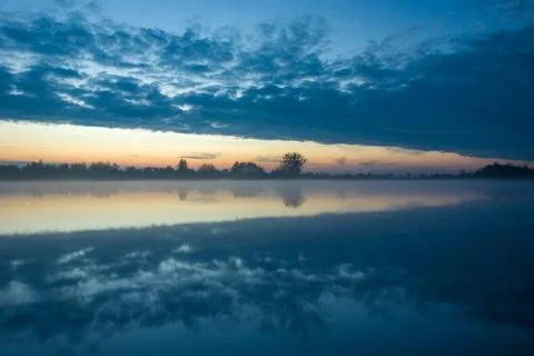 Reflection of the evening clouds in a misty lake Stock Photos