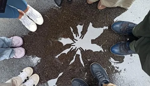 Reflection of friends hands making peace sign in a puddle on wet asphalt Stock Photos