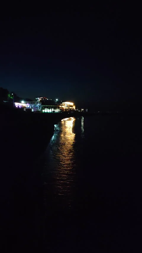 Reflection of glowing lights of buildings on seashore in water sea waves night Stock Footage 269176703
