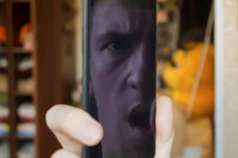 Reflection of half the face of a guy on a smartphone screen, frowned, open mouth Stock Photos