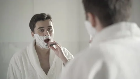 Reflection of handsome brunette man shaving with razor in bathroom. Portrait of Stock Footage 145870604