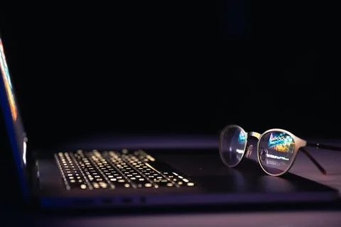 Reflection from a laptop in glasses on a dark background. Stock Photos
