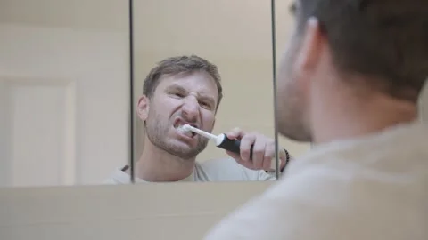 Reflection of a man in a mirror performing his morning dental hygiene routine in 스톡 동영상 335151827