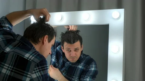 Reflection of man in the mirror unwinds french braids on his head at home. Stock-Footage 167934495