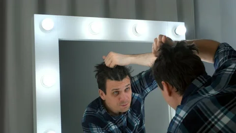 Reflection of man in the mirror unwinds french braids on his head at home. Stock Footage 169527099