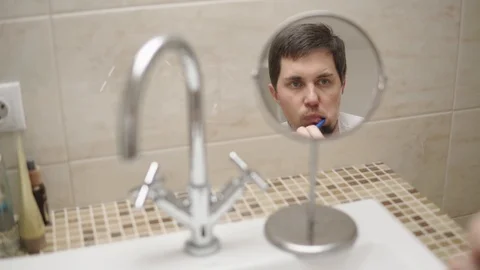 A reflection of a man in the mirror who brushes his teeth in the bathroom Stock Footage 91813153