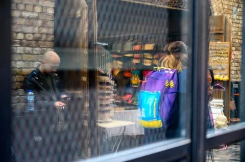 Reflection of a man using a handheld device as shoppers pass by in Camden Mar Foto stock
