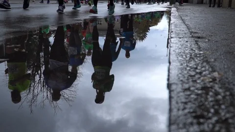 Reflection of marathon runners with man stepping into a puddle in slowmotion 库存影片 97463627