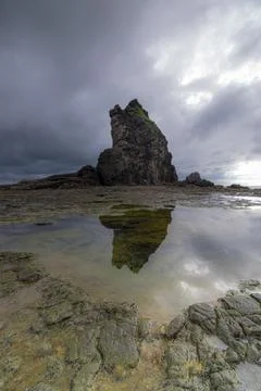 Reflection of a massive rock on a puddle by the beach. Stock Photos