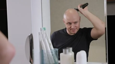 Reflection in the mirror of an adult bald man who shaves his head and beard. Stock Footage 327644294