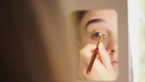 Reflection in a mirror of a girl making up, colouring eyelids with a brush Stock Footage 128520581