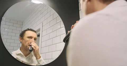 Reflection in the mirror of a young guy shaving with an electric razor, speed Stock Footage 263875421
