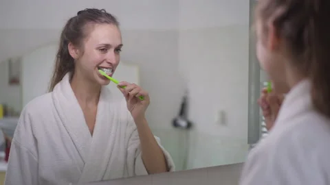 Reflection in mirror of young slim brunette Caucasian woman brushing teeth with Stock Footage 161277437