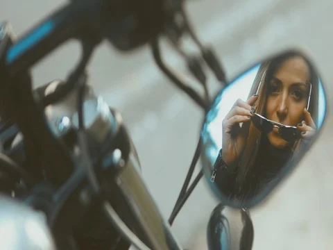 Reflection in motorcycle rear view mirror, female biker putting on sunglasses Stock Footage