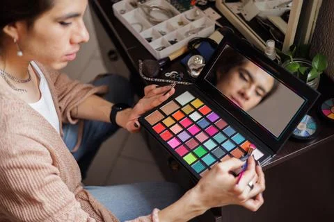 Reflection of a non-binary person in the mirror putting on makeup before goin Stock Photos