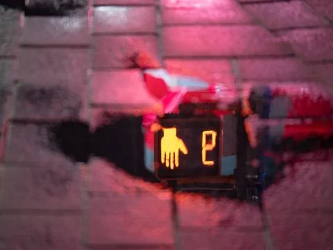 A reflection of orange and red stop sign in a puddle on a rainy night in a br Stock Photos