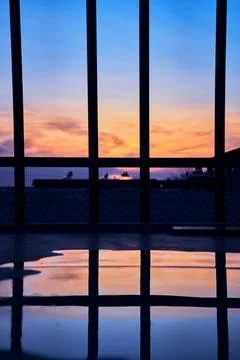 Reflection of Orange Sunset on A Puddle Behind Fences Foto stock