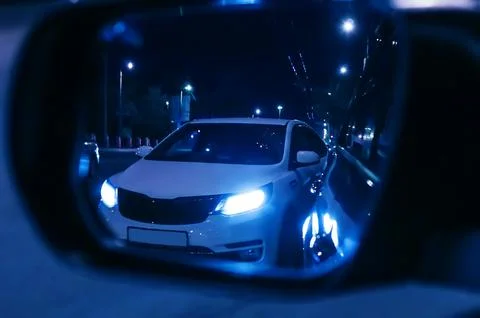 Reflection of overtaking car in rearview mirror. Dark night. Blurred backgrou 库存照片