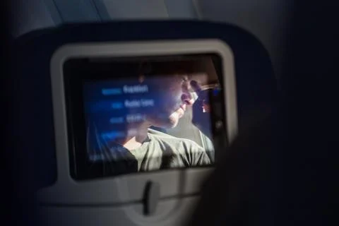 Reflection of a passenger on an airplane touch screen monitor during long flight Stock Photos