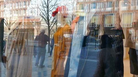 Reflection of people walking in street on the window of a store selling cloths Stock Footage 112080956