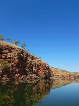 Reflection of a red cliff face with trees in a blue river Stock Photos