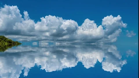 Reflection of rolling white clouds in blue sky on water surface Stock Footage 260477373