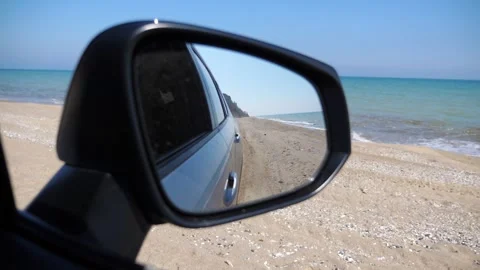 Reflection of serene beach scene in side mirror of parked vehicle, capturing the Видео 332851906