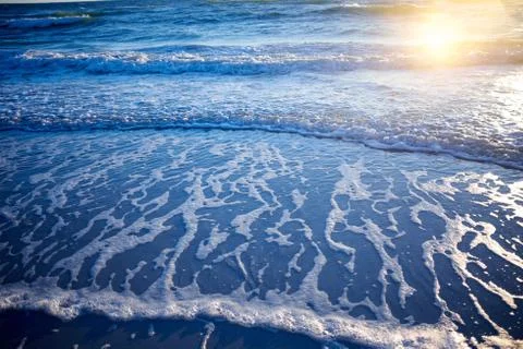 Reflection of the setting sun on a beach with surf Stock Photos