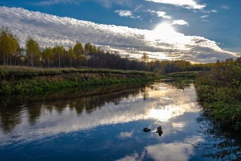 Reflection of the sky with clouds and the sun in the blue water of a small ri Stock Photos