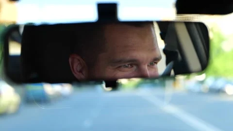 Reflection of smiling male driver on rear-view mirror in car. Cropped, close up Stock Footage 249766335