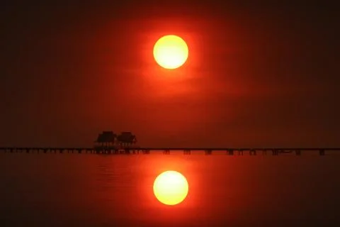 Reflection of sunset back on silhouette bridge and abandon pavillion in sea Photos