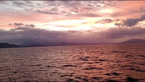 Reflection of sunset light on the ocean with a mountain island in the background Stock Footage 277922133