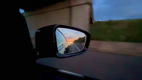 Reflection of the sunset in the rearview mirror of a car. Travel by car. Stock Footage 220222004