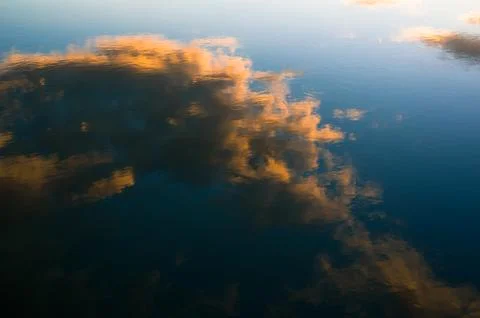 Reflection on the surface of calm water - orange clouds and blue sky during s Foto stock