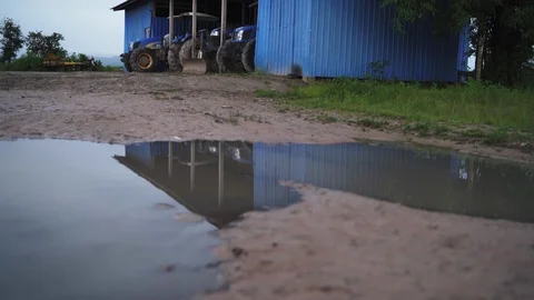 Reflection of tractors in a puddle over a dirt path and a garage in Myanmar Video stock 95620408