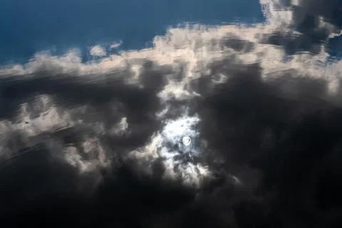 Reflection in the water of a round disk of the sun and a black cloud. Stock Photos