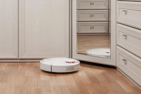 Reflection of white robot vacuum cleaner running before mirror in bedroom. mo Stock Photos