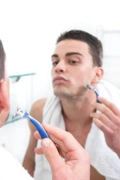 Reflection of young man shaving in bathroom mirror Stock Photos