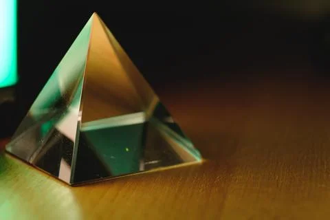 Reflections and light play within a glass prismatic pyramid on a wooden table Stock Photos