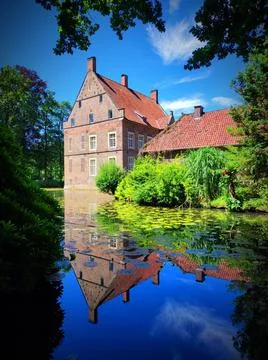 Reflections of a historic building by a pond surrounded by trees on a clear.. Stock Photos