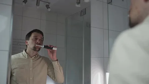Reflections in mirror, man in shirt before work brushes his teeth with black Video stock 287933091