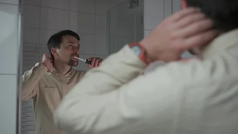 Reflections in mirror, man in shirt before work brushes his teeth with black Video stock 295324600