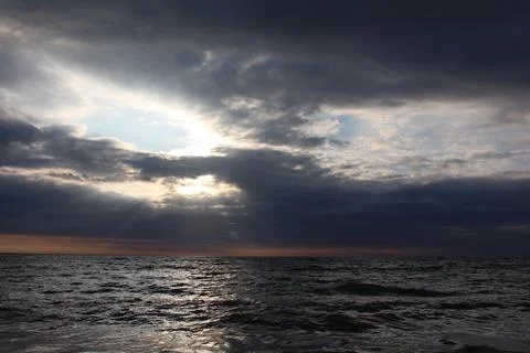 Reflections of the sun in the sky. Sunbeams through dark clouds. Seascape. Stock Photos