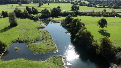 Reflective pond surrounded by green fields, trees, mountains in distance. Stock Footage 287114171