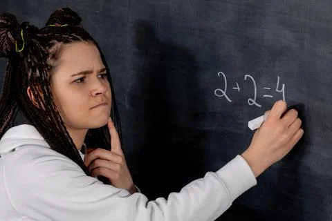 A reflective student solving a complex math problem on a chalkboard with Stock Photos